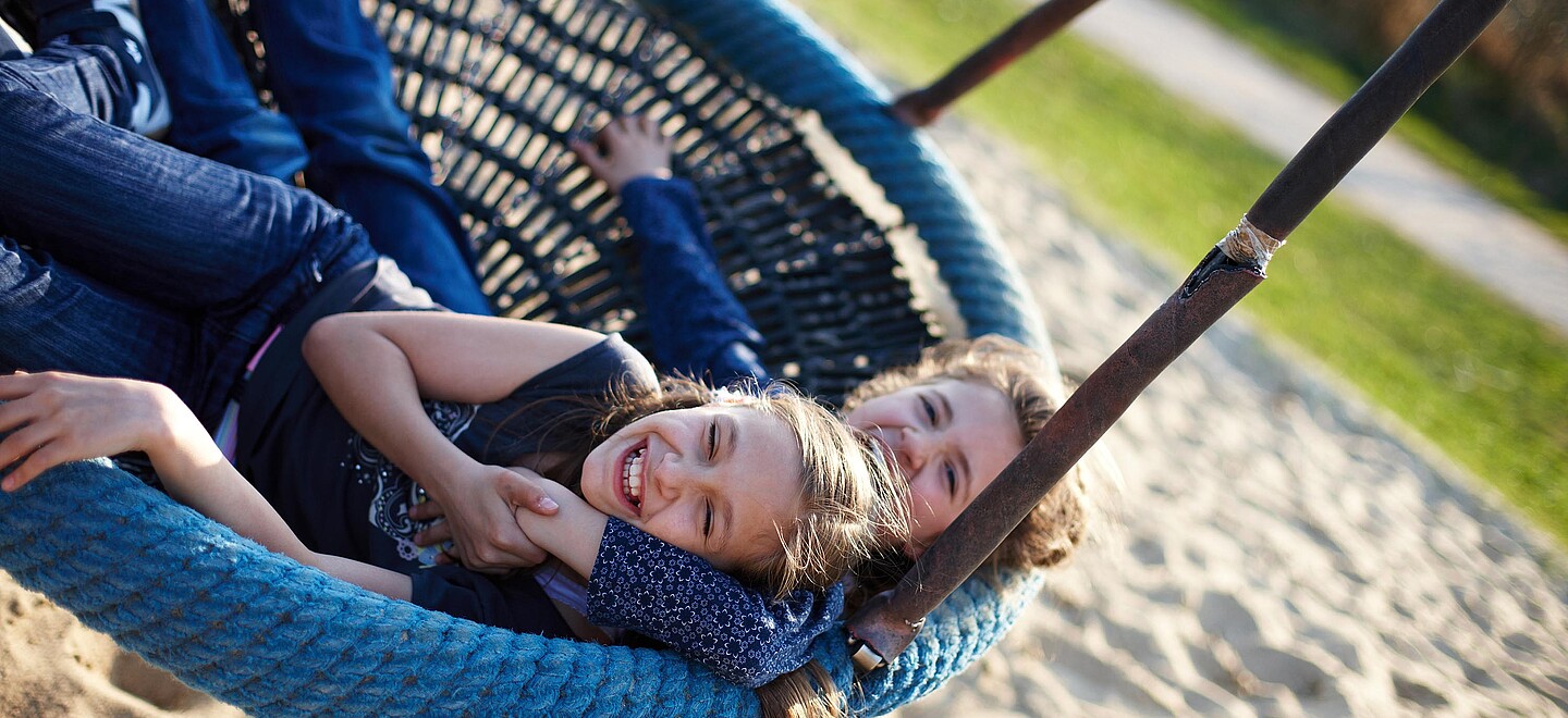 Zwei Mädchen schaukeln auf einer Nestschaukel und lachen miteinander.