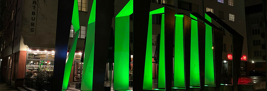 Geometrische Skulptur aus Beton und Stahl vor dem heutigen Café Lichtburg nachts im grünen Licht.