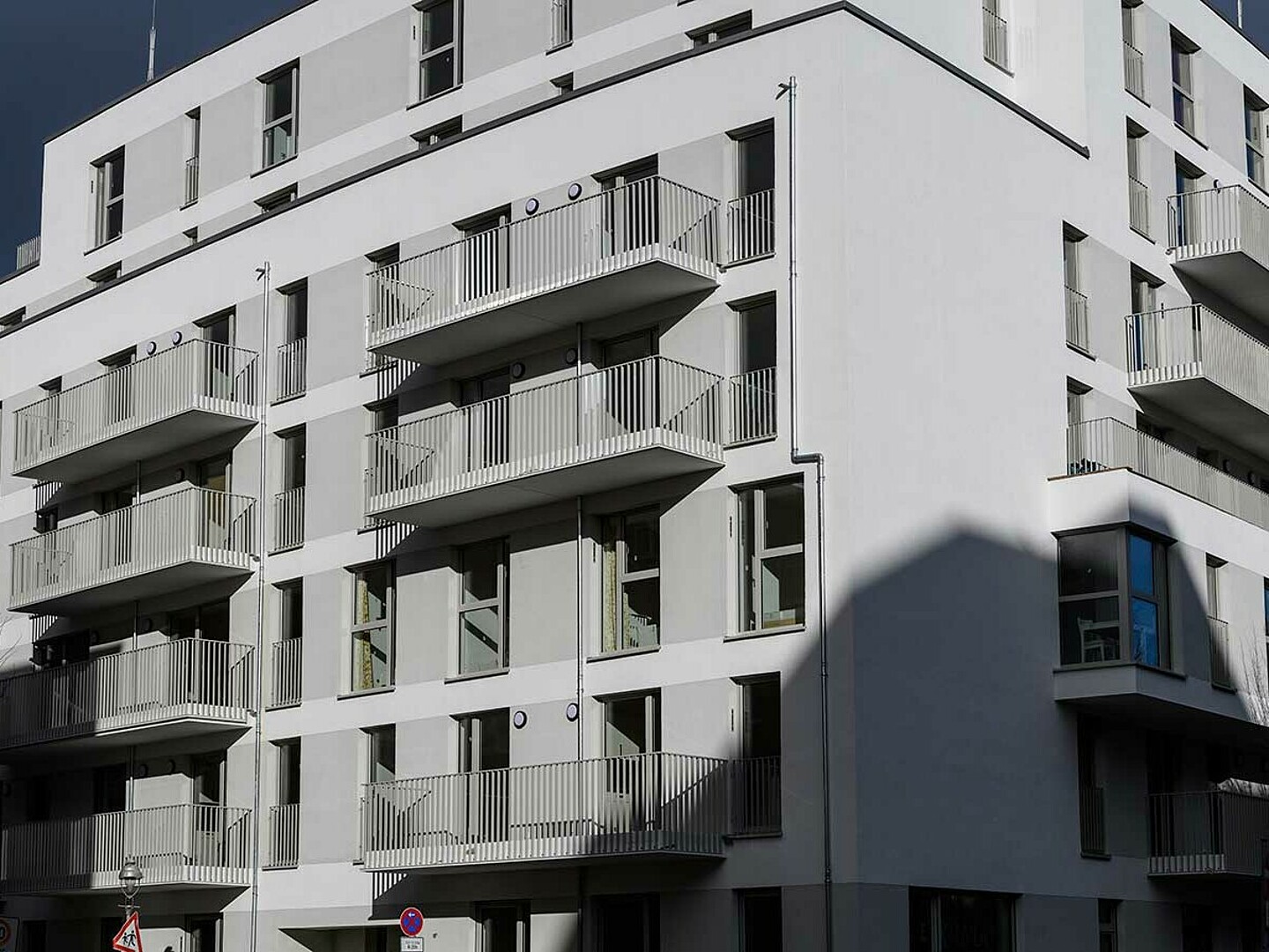 An einer Straßenkreuzung steht ein Neubau mit einer weißen Fassade und Balkonen.