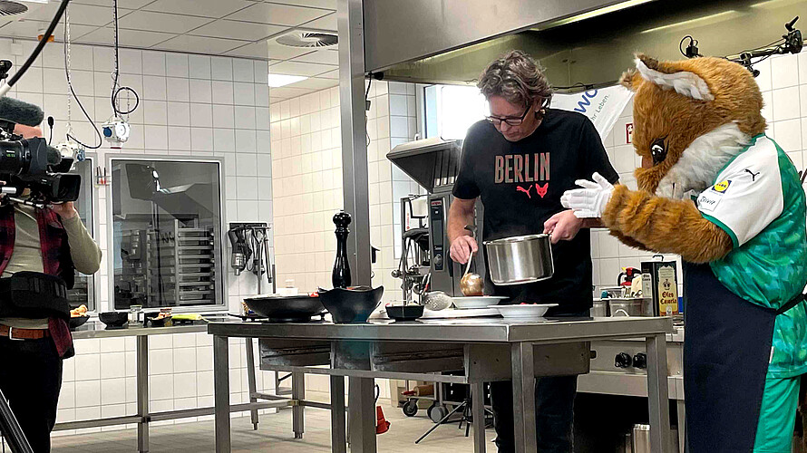 Maskottchen Fuchsi und ein Mann kochen zusammen.