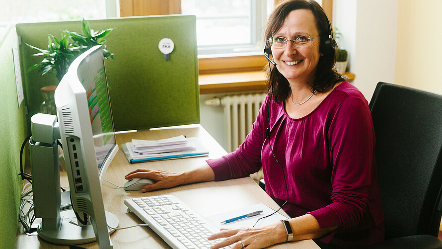 Frau sitzt am Schreibtisch vor einem Computer.