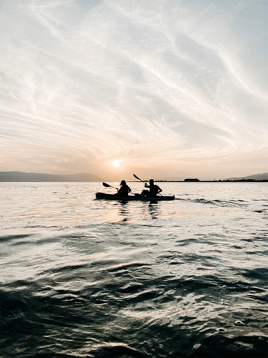 Zwei Personen rudern in Kanus auf dem Wasser in der Abendsonne.
