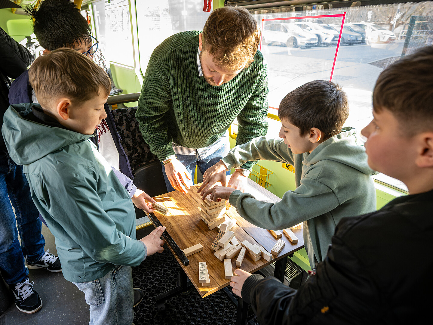 Vier Kinder und ein Mann stehen um einen kleinen Tisch im Demokratie-Mobil und stapeln Holzsteine auf einen Jenga-Turm.