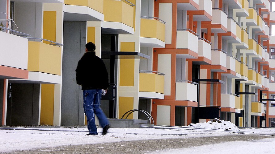 Wohnanlage im Winter mit gestreutem Fußgängerweg. Ein Mitarbeiter läuft den Weg ab.