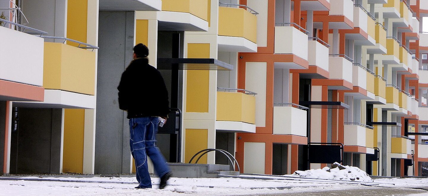 Wohnanlage im Winter mit gestreutem Fußgängerweg. Ein Mitarbeiter läuft den Weg ab.
