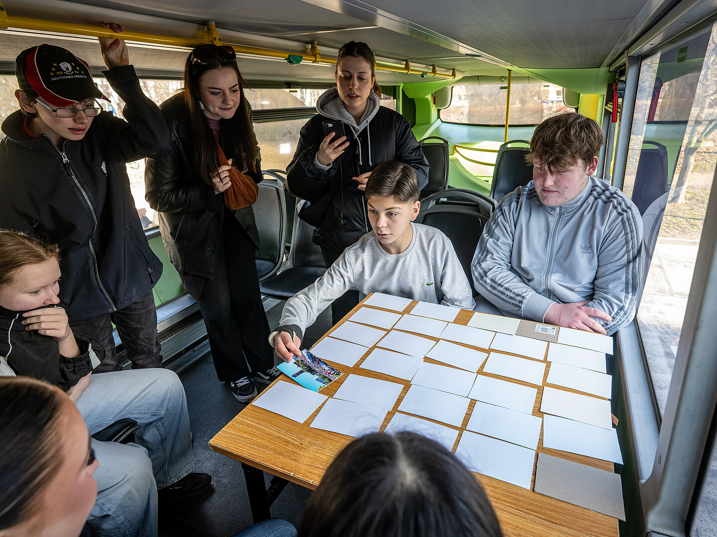 Eine Gruppe Jugendlicher sitzt um einen Tisch mit umgedeckten Karten im Demokratie-Mobil. Ein Junge dreht eine der Karten um.