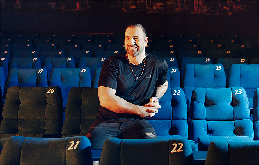 Emanuel Fernandes vom Thalia Kino in Berlin Lankwitz sitzt in einem Kinosessel und freut sich.