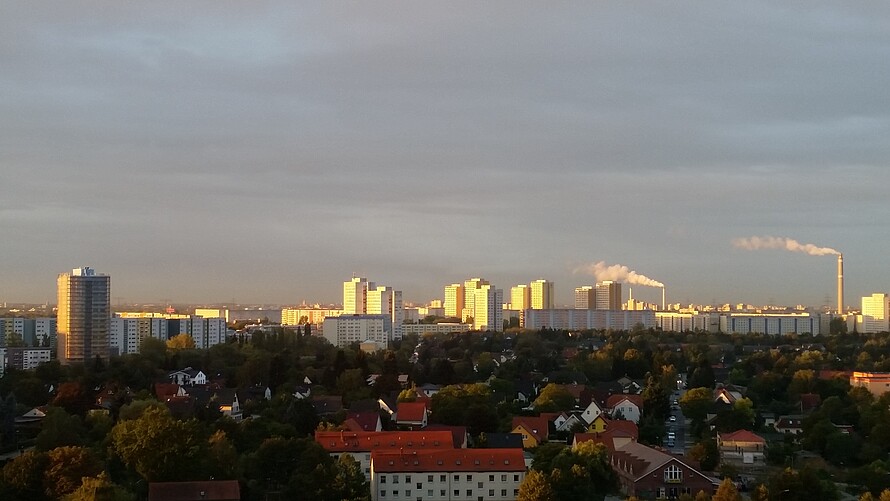 Ein Panorama-Foto von einem Ausblick auf Berlin. Zu sehen sind Hochhäuser vom Helene-Weigel-Platz, das Dorf Alt-Marzahn, Mehrfamilienhäuser, Bäume und Fabrikschornsteine.