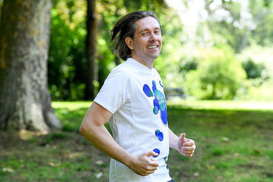 degewo Mitarbeiter Christoph Schneider joggt in einem Park in Berlin. Dabei lächelt er in die Kamera.
