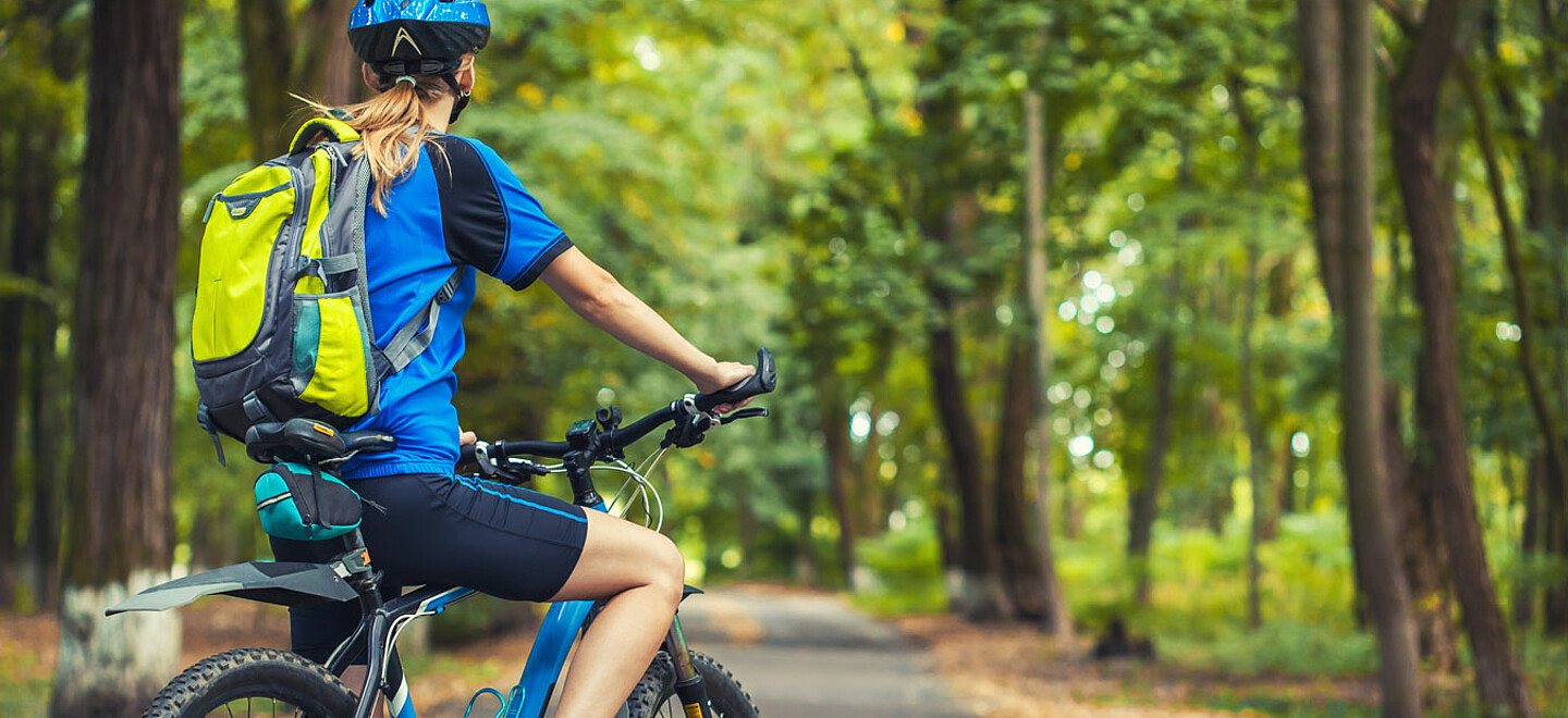 Frau fährt mit dem Fahrrad durch einen Wald.