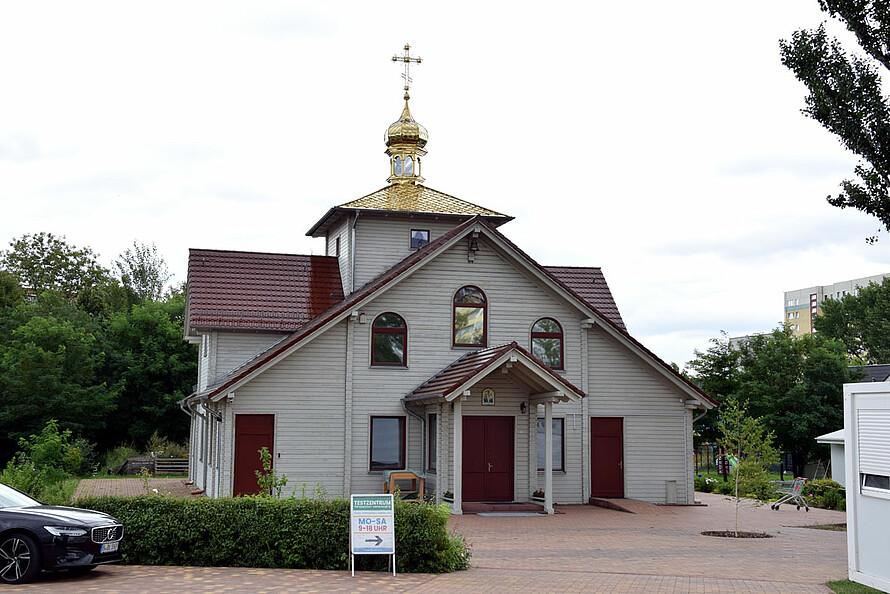 Russische Orthodoxe Kirche vor vielen Bäumen und Grünen. Links gibt es ein Auto