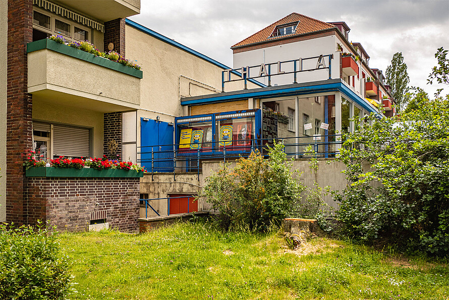 Blick in einen grünen Hof auf mehrere Wohnungen mit Balkon und ein Kino (mit „Thalia“-Schriftzug auf dem Dach)