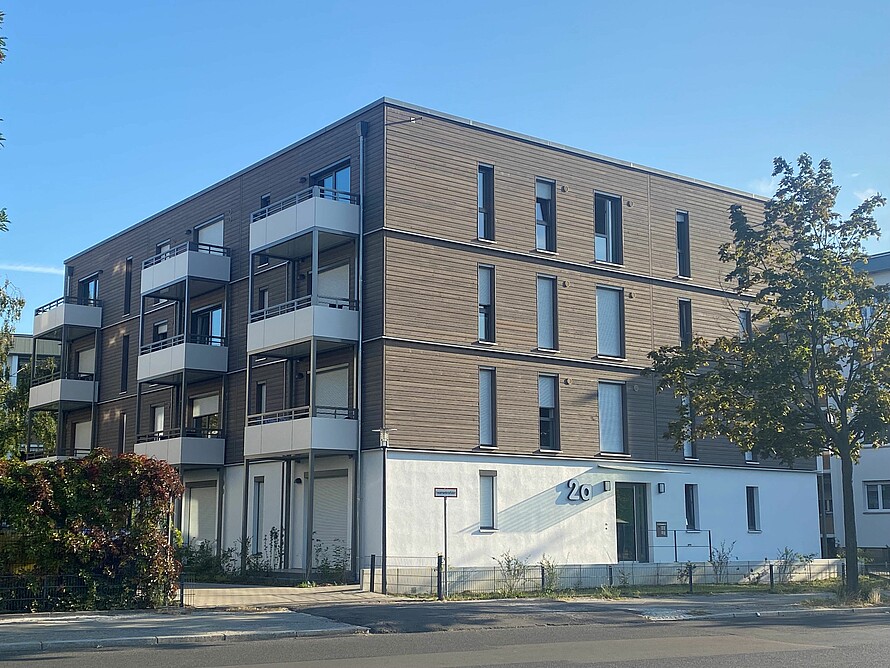 Blick auf ein Mehrfamilienhaus mit dunkelbrauner Fassade.