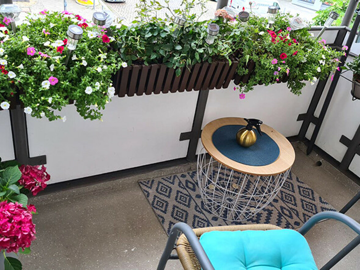 ein mit vielen kleinen Topfpflanzen dekorierter Balkon. Auf dem Balkon stehen zwei Holzstühle.