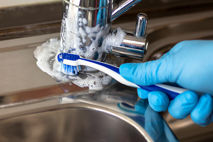 Mit einer Zahnbürste wird der Wasserhahn gebürstet.