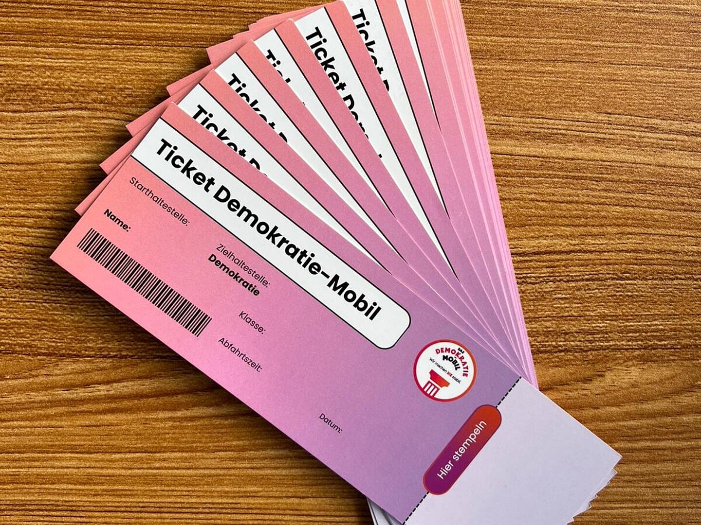 Mehrere rosafarbene Tickets mit der Aufschrift "Ticket Demokratie-Mobil" fächerförmig auf einem Holztisch ausgelegt.