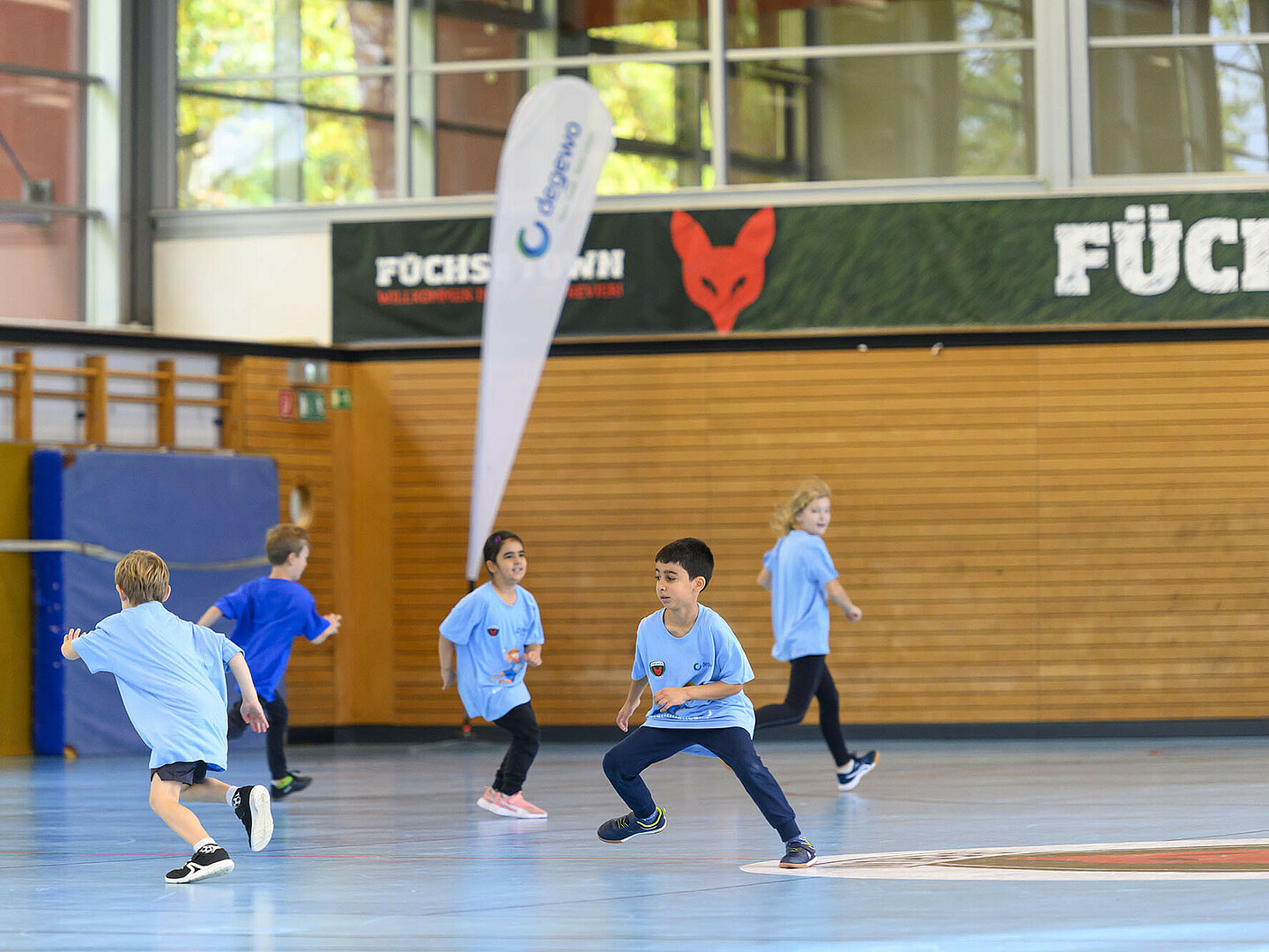Fünf Kinder in blauen Trikots rennen durch eine Sporthalle.