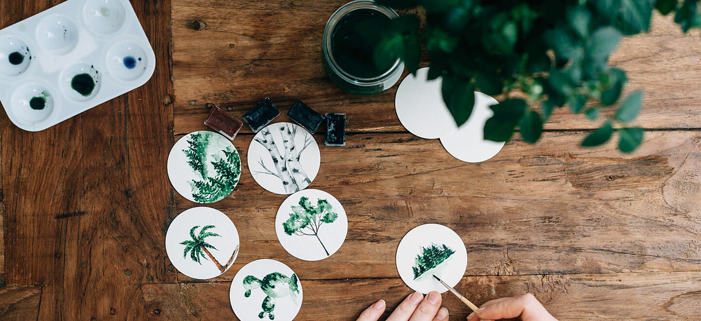 Kleine runde Bilder werden mit Wasserfarbe bemalt mit Baummotiven.