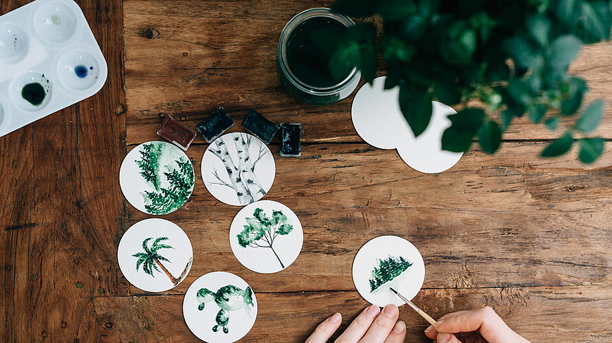Kleine runde Bilder werden mit Wasserfarbe bemalt mit Baummotiven.
