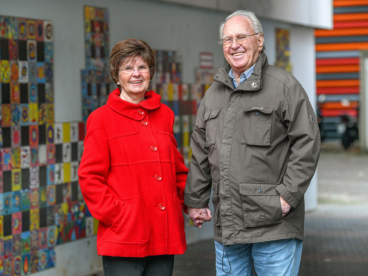Bärbel und Udo Schulte stehen vor einer Wand mit farbenfrohen Fliesen und halten sich an den Händen.