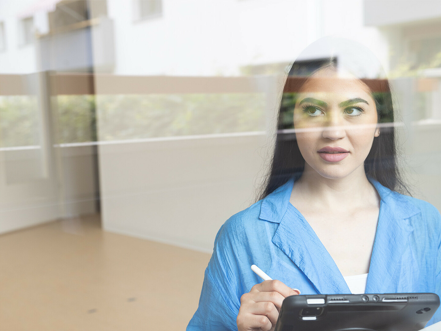 Person schaut durch ein Fenster. In der Hand hält sie ein Tablet und einen Stift.