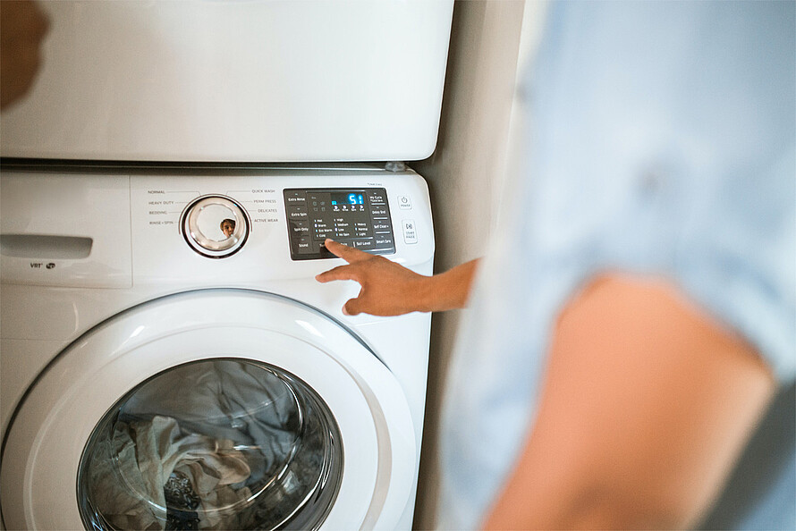 Eine Waschmaschine voller Wäsche wird von einer Person bedient.