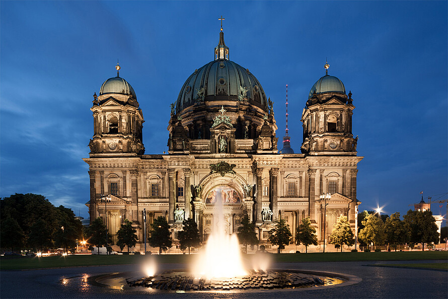 Im Fokus steht eine große Kathedrale im Stil der Neorenaissance und des Neobarock, die bei Nacht beleuchtet wird.