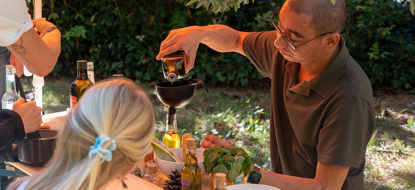 Ein Mann steht hinter einem Tisch und füllt eine Flüssigkeit über einem Trichter ab. Auf dem Tisch befinden sich verschiedene Gefäße stehen. Er