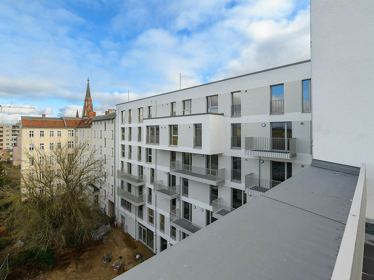 Der Blick geht von einem Balkon auf die gegenüberliegende Seite eines Neubaus.