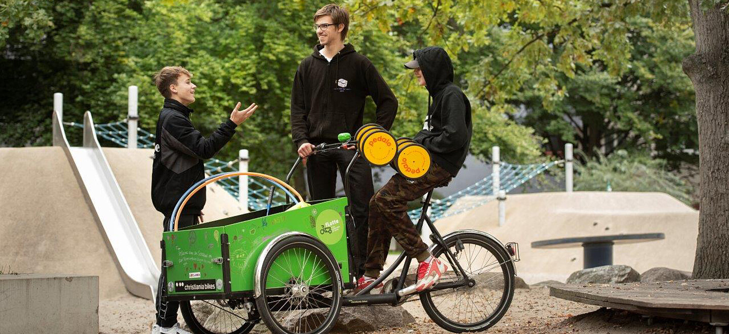 Mann und Jungs unterhalten sich, Junge sitzt auf Lastenrad.