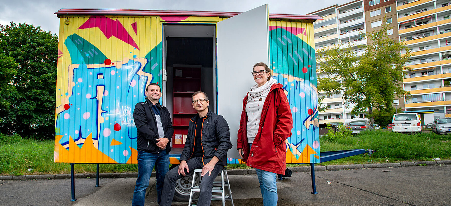 Drei Personen stehen vor einem bemalten Container.