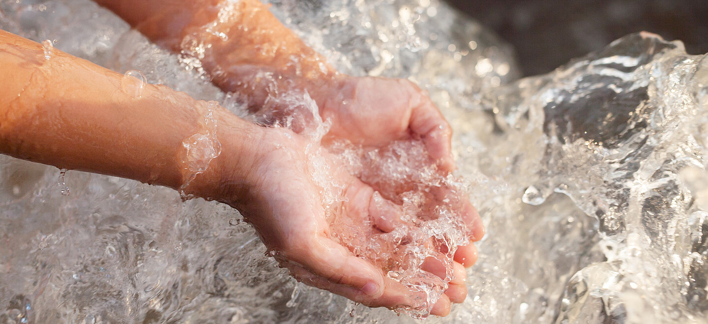 Zwei Kinderhände fangen literweise Wasser auf.