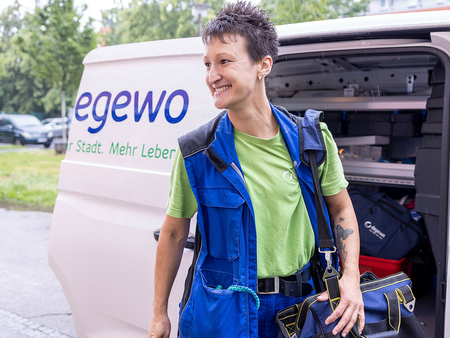 Person steht vor einem Auto mit der Aufschrift "degewo" und lächelt.