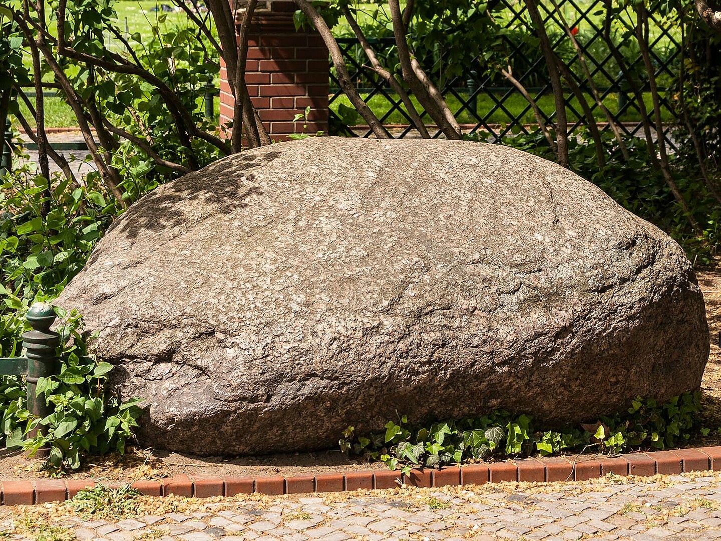 Ein rotbrauner großer Stein am Wegrand.