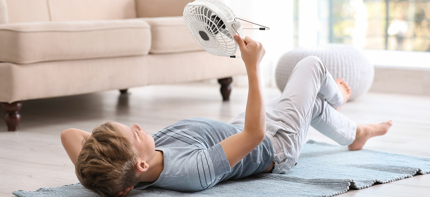 Junge liegt auf dem Boden und richtet einen Ventilator auf sich