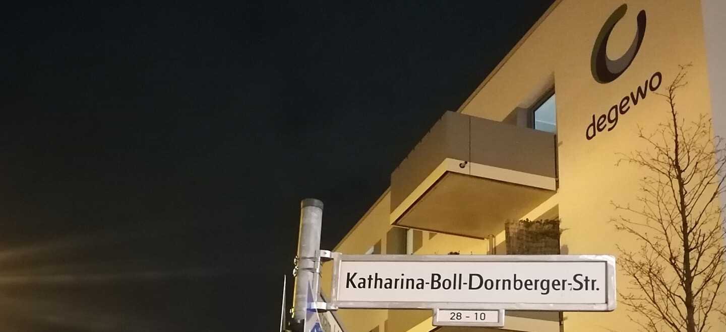Das Straßenschild der Katharina-Boll-Dornberger-Straße. Das Logo von degewo ist auf einem Haus im Hintergrund zu erkennen.