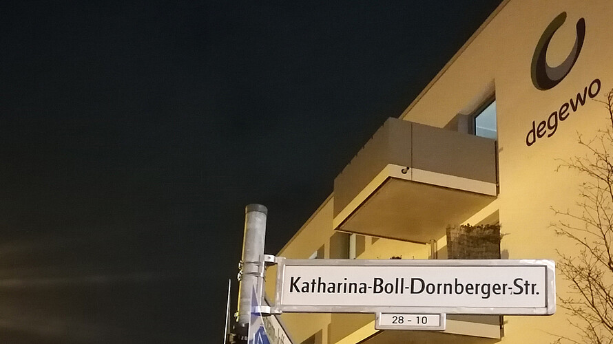 Das Straßenschild der Katharina-Boll-Dornberger-Straße. Das Logo von degewo ist auf einem Haus im Hintergrund zu erkennen.
