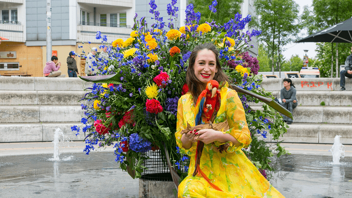Frau sitzt mit Papagei auf dem Arm vor dem Flowerflash