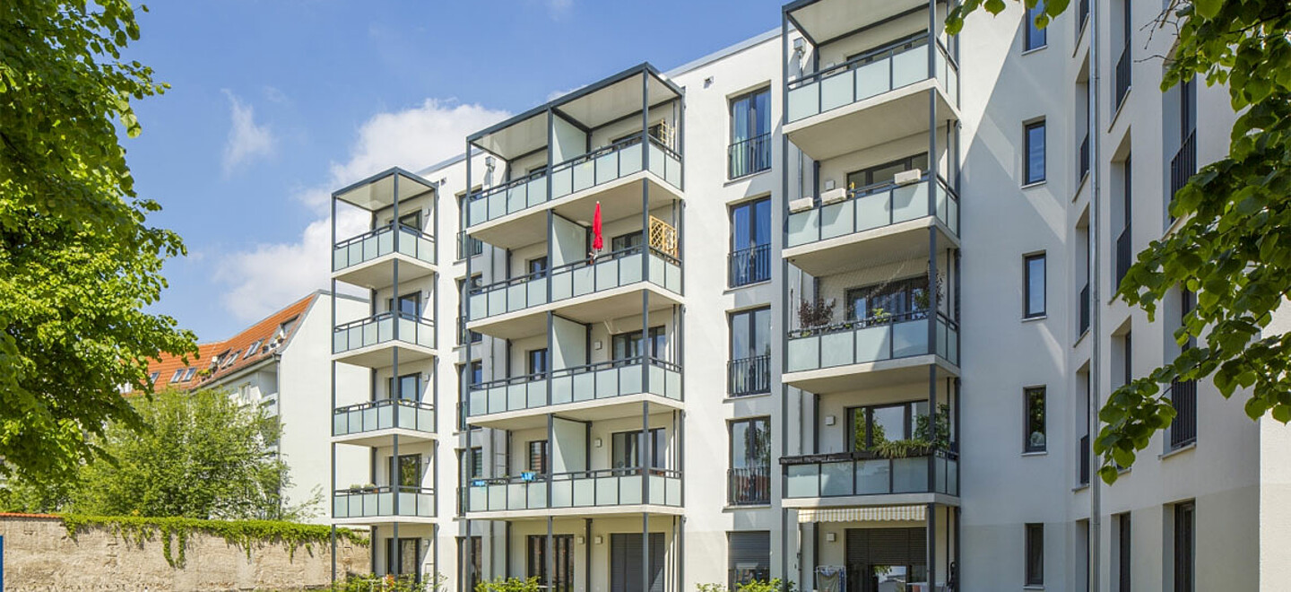 Blick auf ein mehrgeschossiges Wohnhaus mit Balkonen bei Sonnenschein.