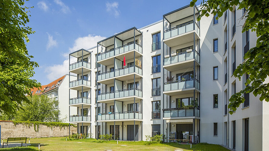 Blick auf ein mehrgeschossiges Wohnhaus mit Balkonen bei Sonnenschein.