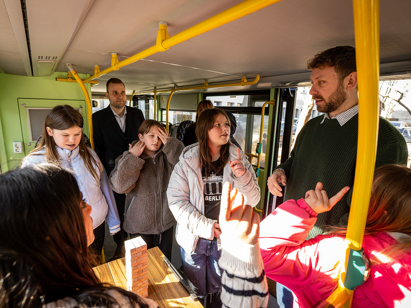 Eine Gruppe Kinder und zwei Erwachsene stehen im Demokratie-Mobil und spielt Demokratie-Jenga. Zwei der Kinder melden sich.