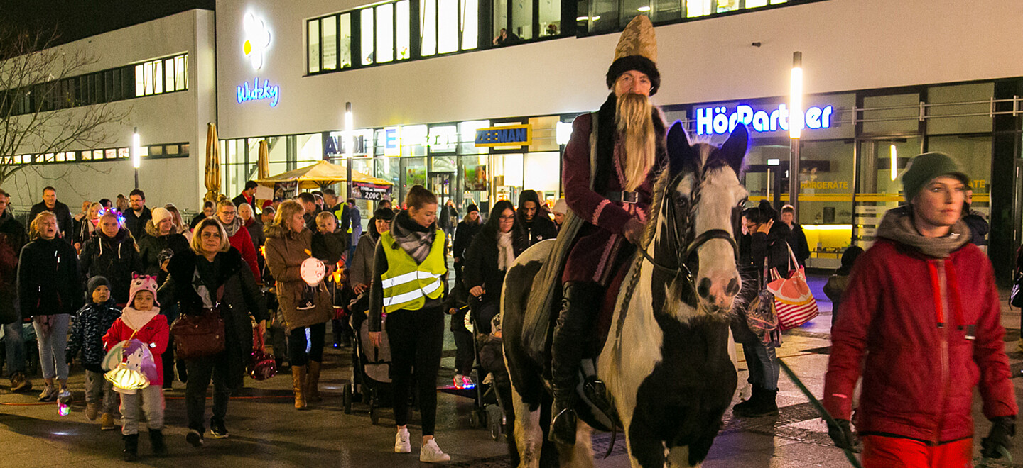 Menschenmenge läuft einem Mann, verkleidet als Sankt Martin auf einem Pferd sitzend, hinterher.