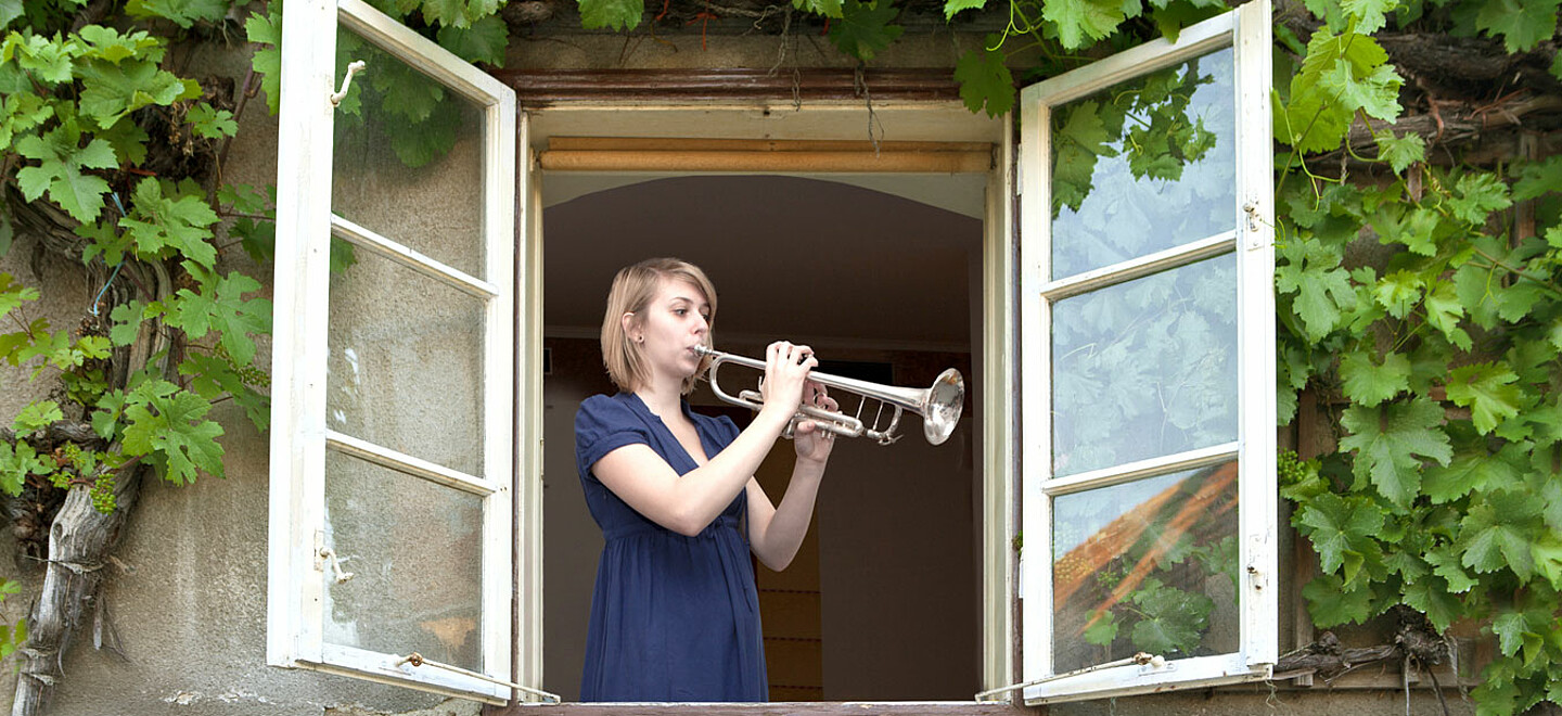 Frau spielt am offenem Fenster Trompete