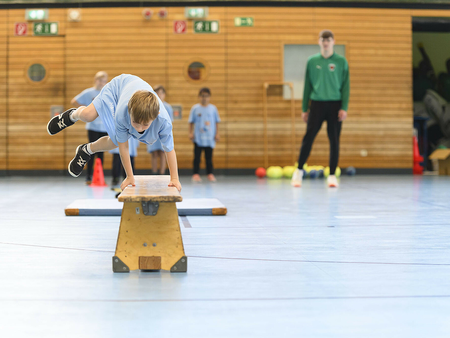 Ein Kind springt über einen Barren in einer Sporthalle.