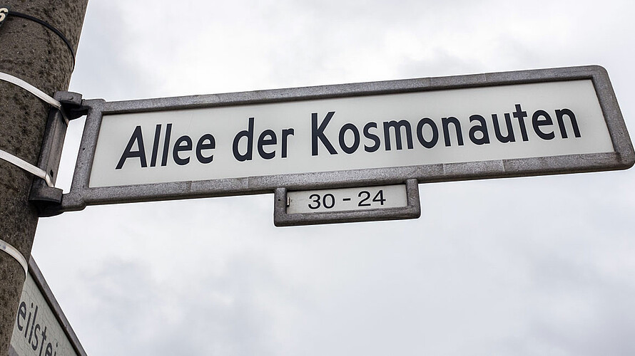 Strassenschild Alle der Kosmonauten: Schriften in schwarz vor dem weißen Hintergrund
