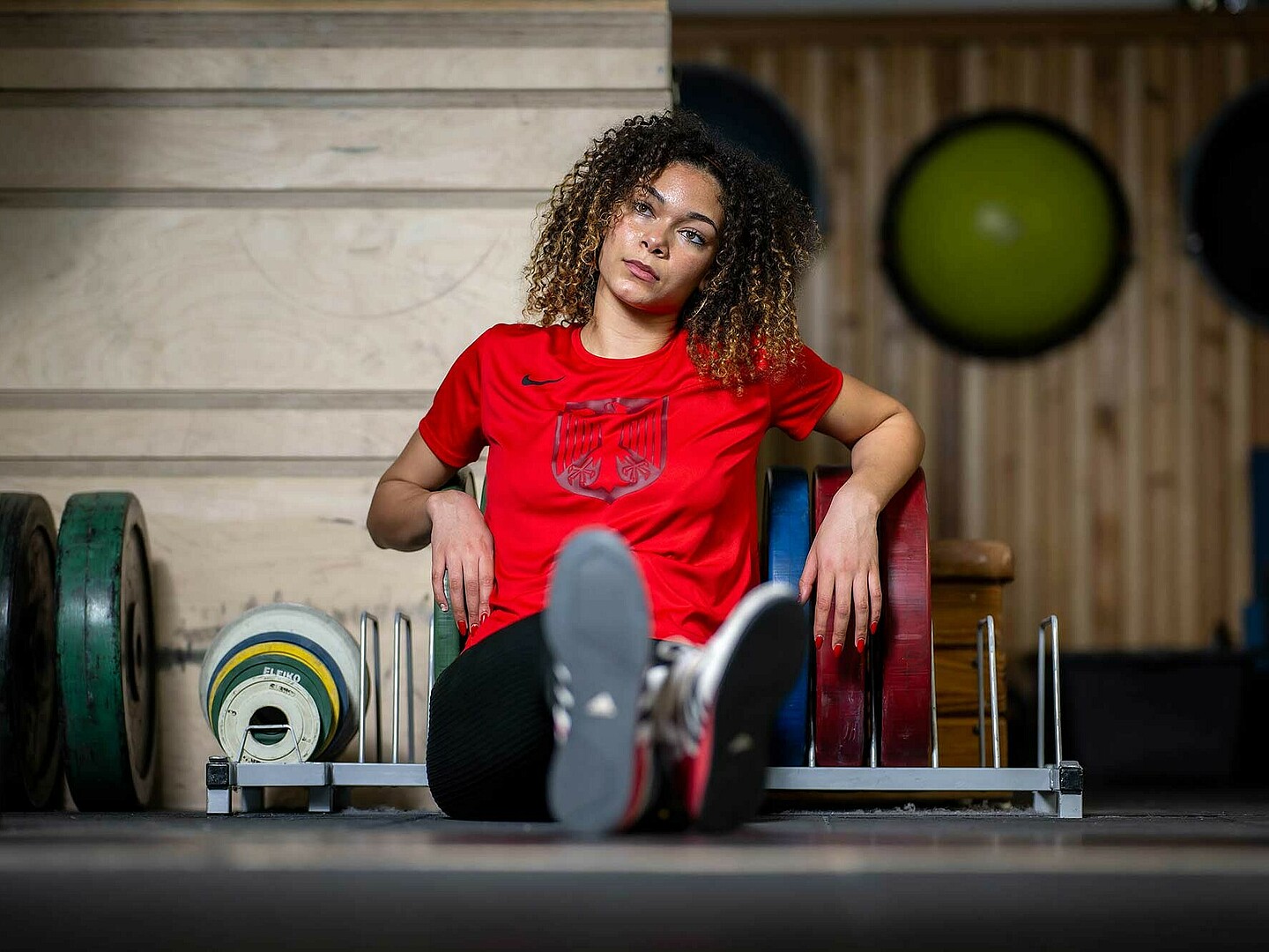 Eine junge Hammerwerferin sitzt auf dem Boden des Sportraums und schaut nachdenklich in die Ferne.