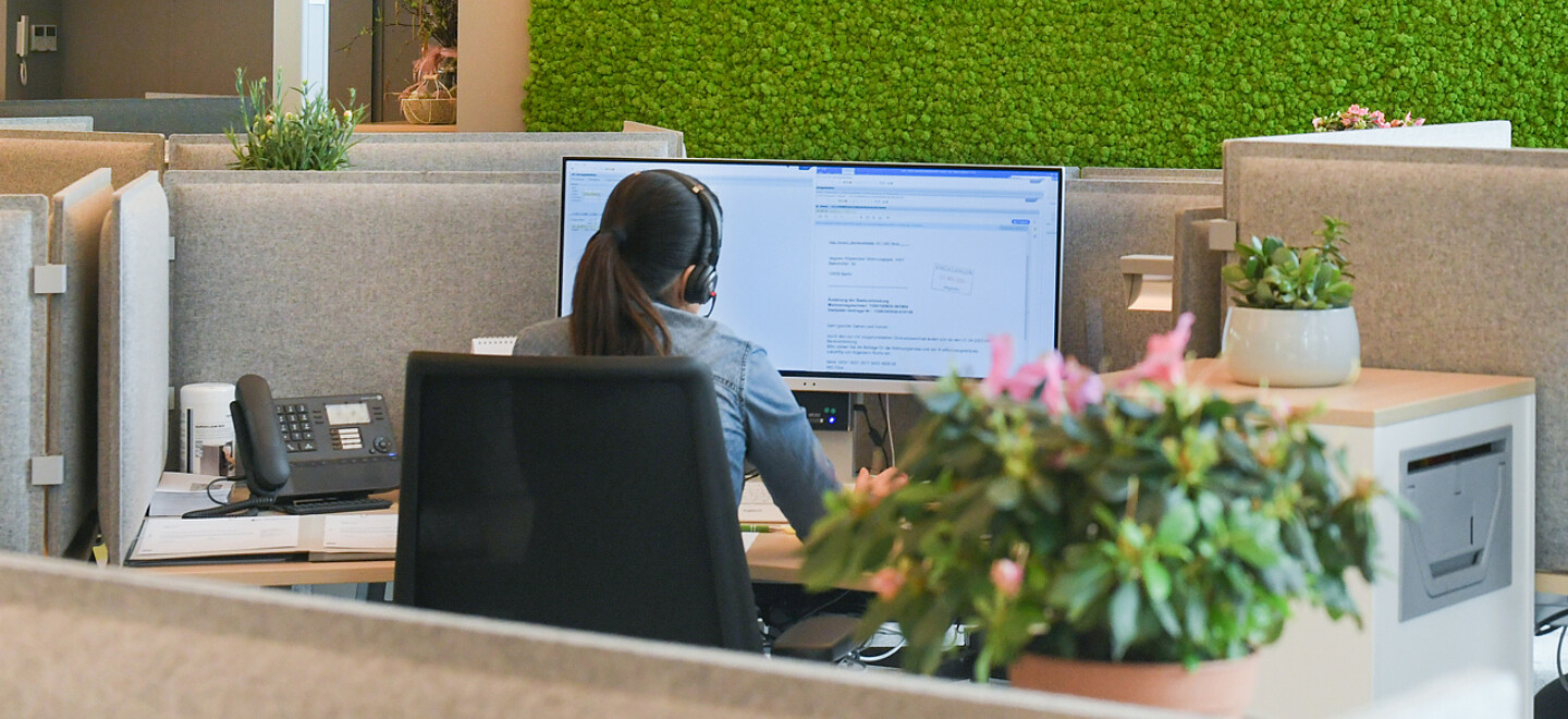 Frau sitzt im Büro mit Headset am Computer.