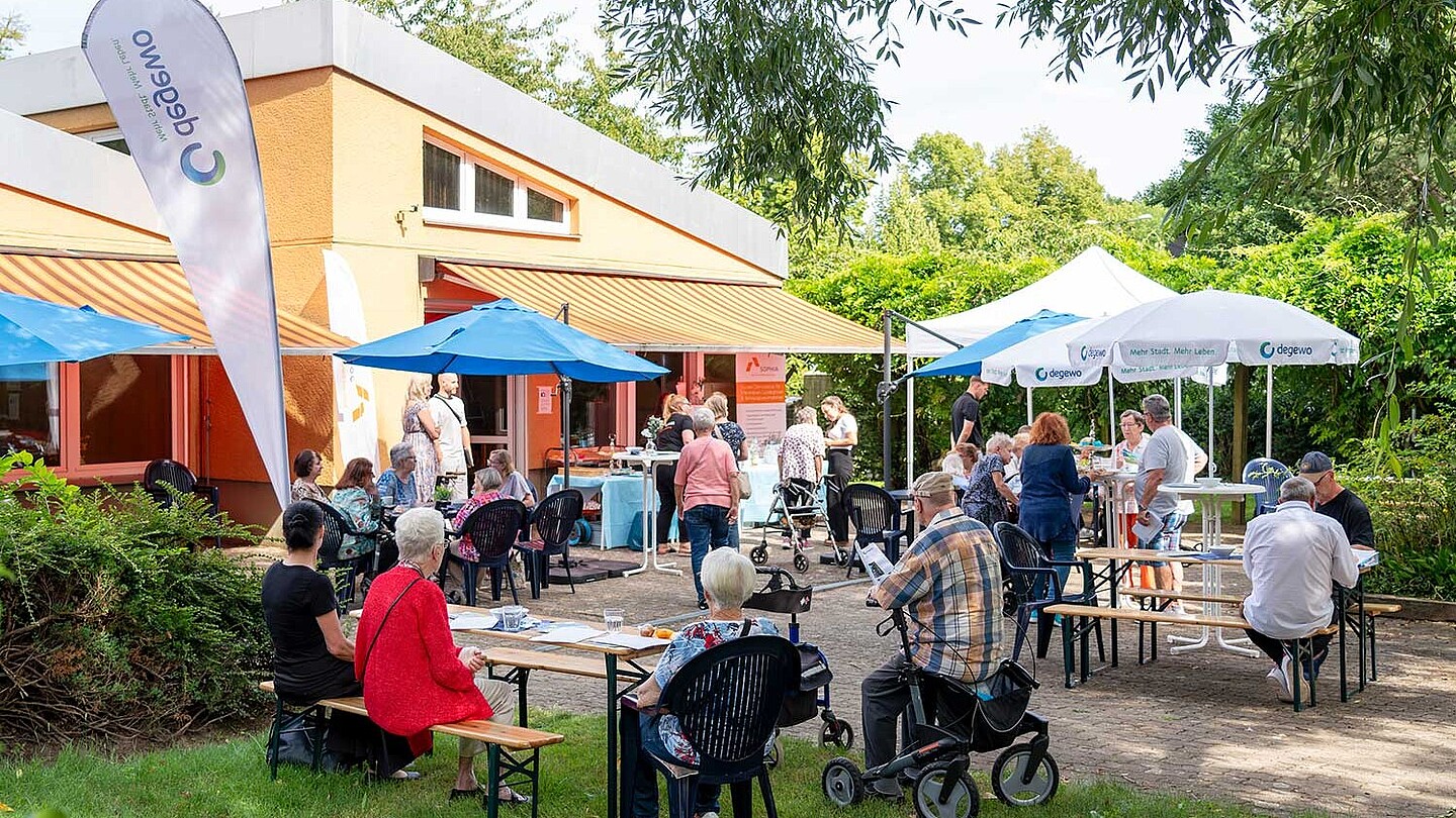 1. Sanierungscafé in der Horstwalder Straße: Die Anwohner sitzen in einem Garten auf Bierbänken an Tischen und lassen sich informieren.