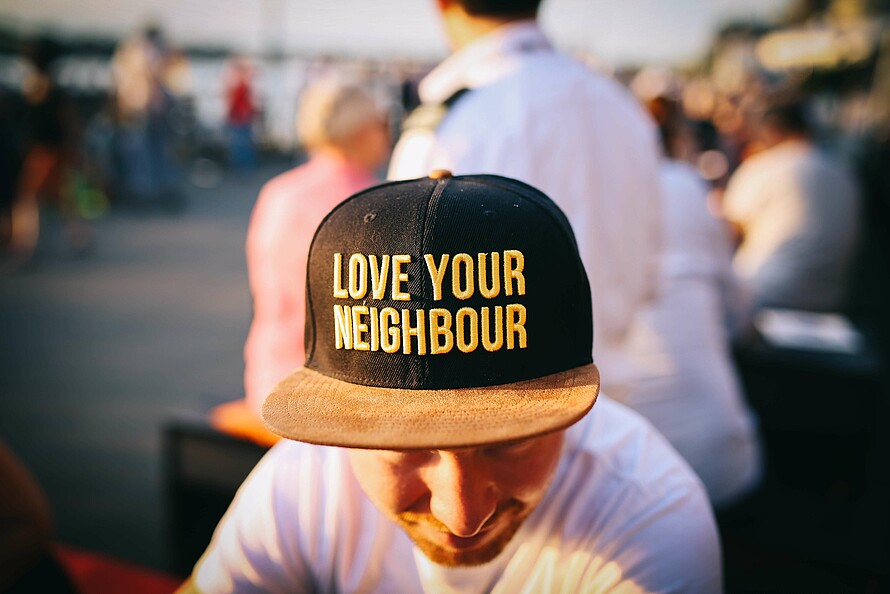 Ein Mann trägt eine Kappe, auf der auf Englisch steht "Liebe deinen Nachbarn"