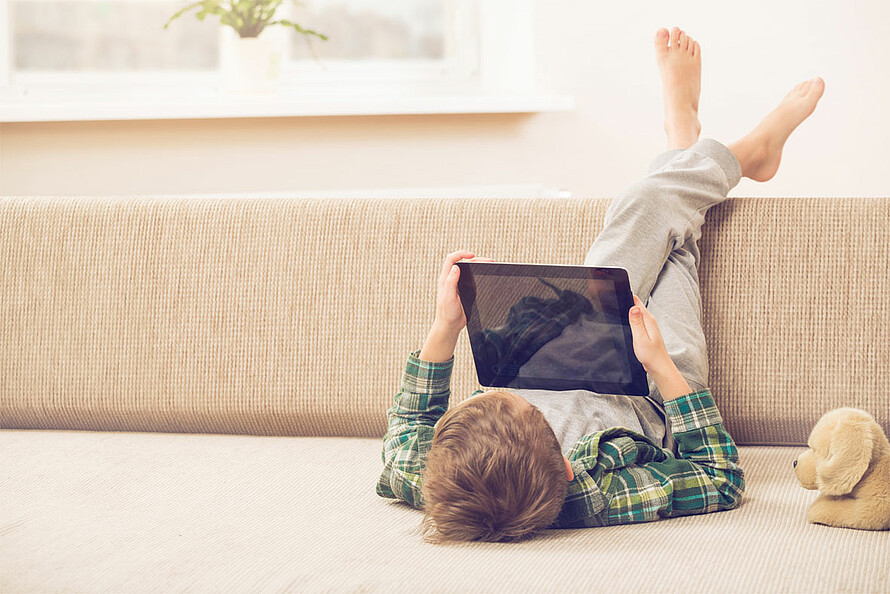 Ein Kind liegt auf dem Boden und schaut auf ein iPad